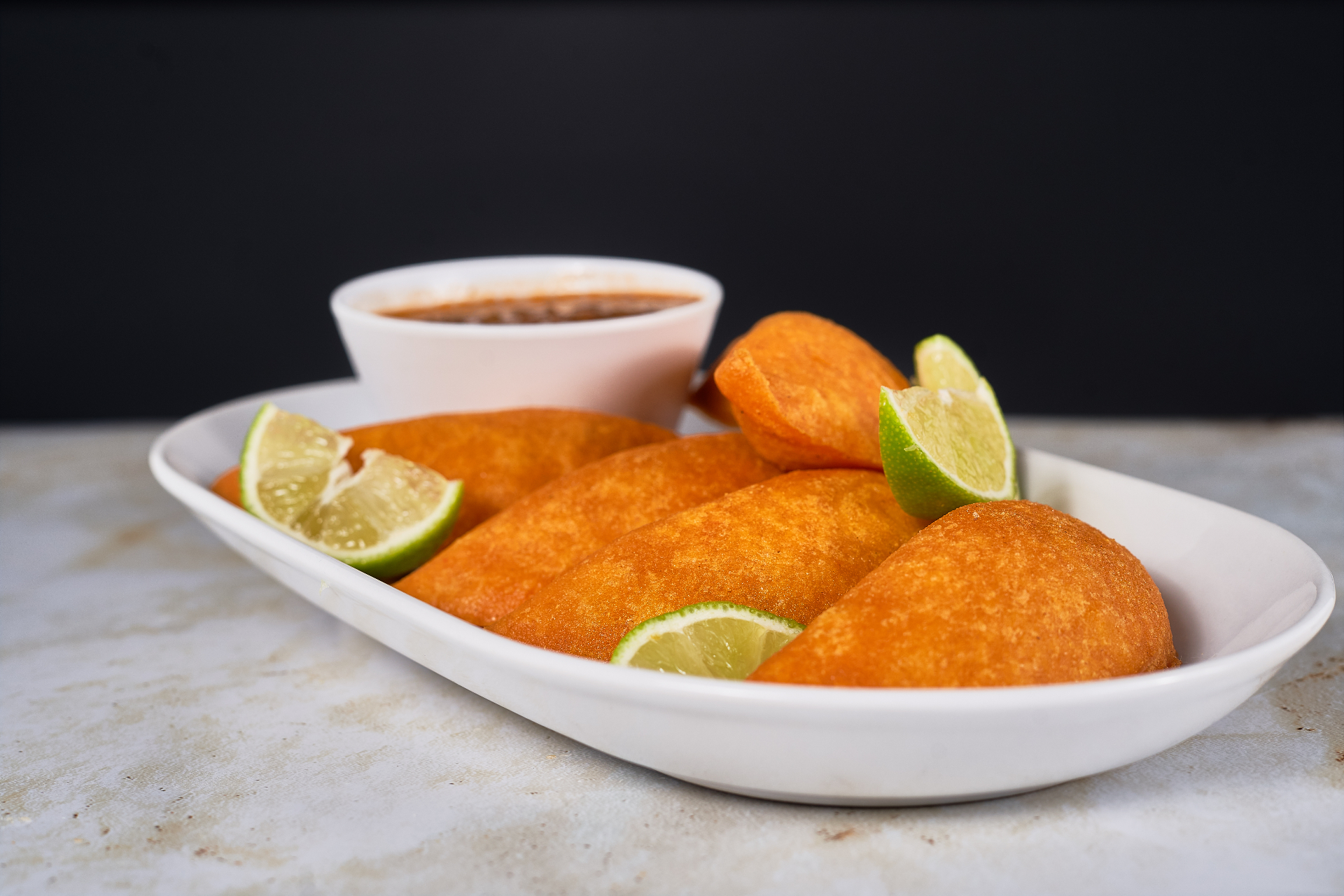 Golden empanadas served with lime wedges and sauce